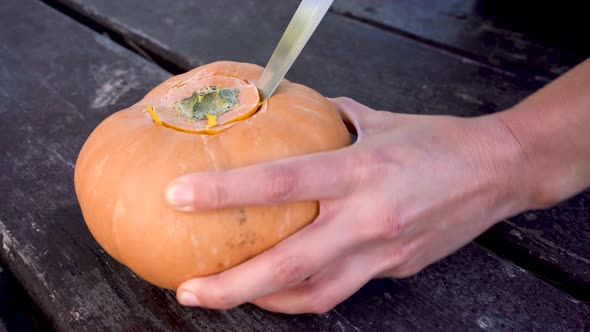 Hands cutting off the lid of a pumpkin, preparing evil pumpkin for Halloween