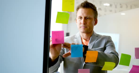 Businessman writing on sticky note on glass wall 