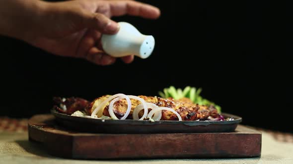 Close-Up Roasted Chicken BBQ Sprinkle With Salt Male Hand Black Background.