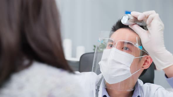 Asian specialist male doctor use flashlight on patient eye in hospital.