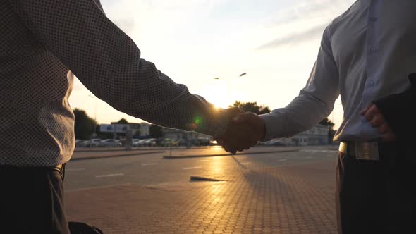 Arm of Male Business Man Passing a Black Briefcase To His Partner. Colleagues Shake Hands Outdoor in