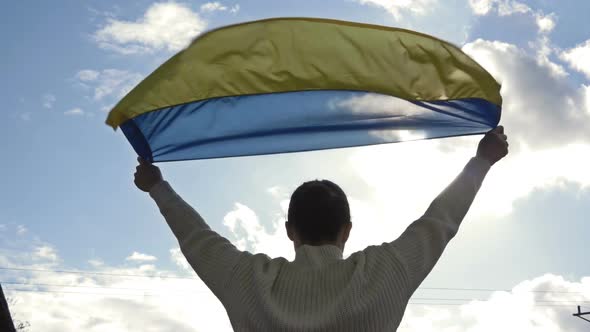 Woman Holds a Waving Flag of Ukraine Against a Blue Sky