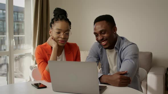 African American Couple Laughing and Discussing Their Plans Using a Laptop in the Apartment