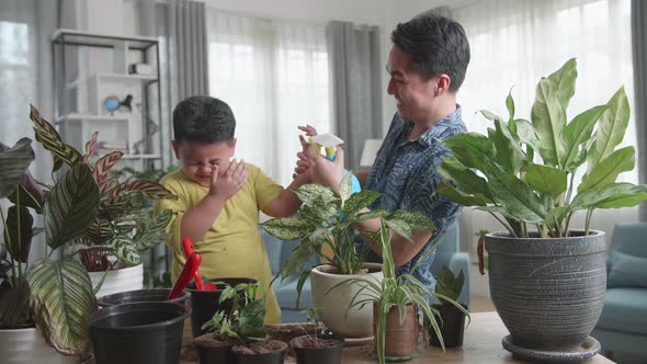 Happy Father And Son Taking Care Of Home Plants At Table Indoors