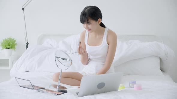 Beauty of young asian woman with learning makeup with brush on cheek on laptop computer.