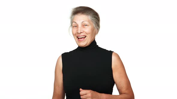 Older Lady with Grey Tied Hair Looking at Camera Smiling with White Teeth Showing Thumb Up Over