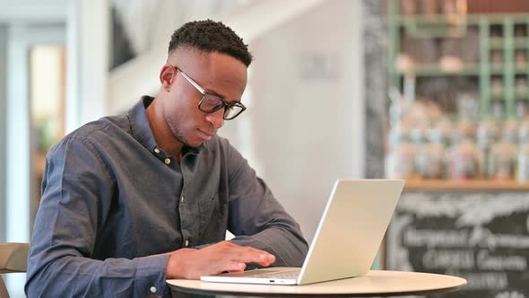 African Man Thinking and Working on Laptop in Cafe 