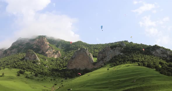 Paragliding Pilots Fly Paragliders Among Clouds and Green Mountains