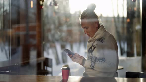A Homosexual Man is Sitting in a Cafe with a Mobile Phone Behind the Glass