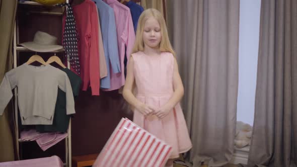 Portrait of Joyful Caucasian Blond Girl in Pink Dress Standing at Home with Shopping Bag