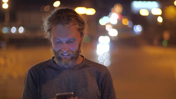 Close Up Portrait of a Handsome Caucasian Bearded Long-haired Young Man with Smartphone Inviting