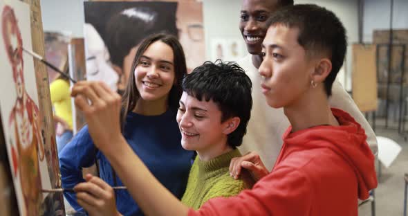 Multiracial students painting together inside art classroom at university