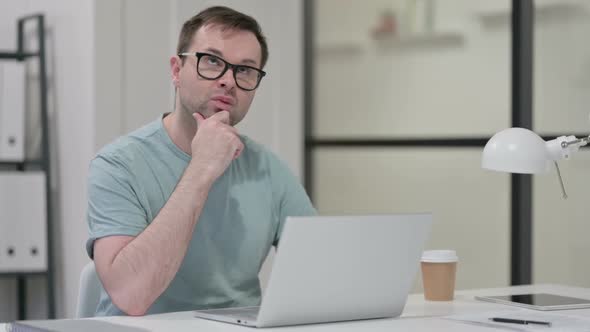 Young Man with Laptop Thinking at Work