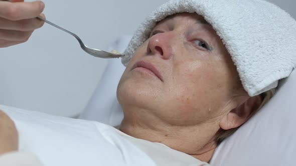 Crying Old Woman With Towel on Forehead Refusing Food From Volunteer, Care