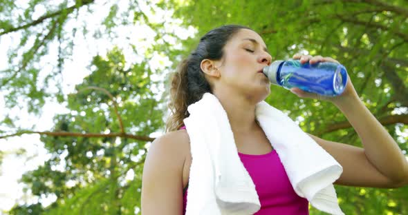 Woman wiping her brow and drinking water after workout in the park