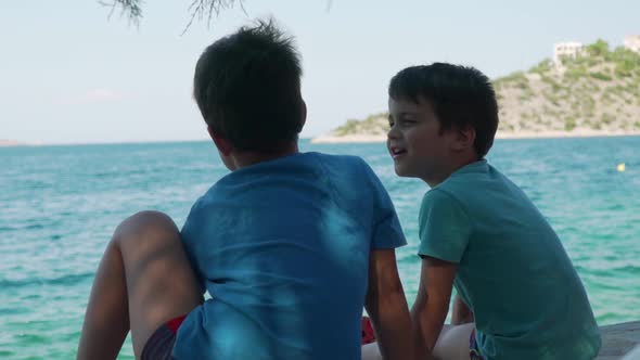 Slow motion of two caucasian kids brothers, talking to each other and staring at the sea. Fragoliman