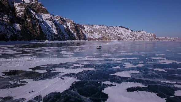 Flying of a Drone Over the Ice of the Lake Behind a Driving Car Along the Rocky Coast
