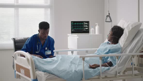 A Male Doctor is Talking to a Patient Lying on a Hospital Bed in a Hospital Ward