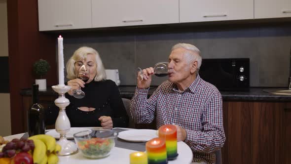 Portrait of Senior Old Couple Toasting Wine at Home During Romantic Supper in Kitchen at Home