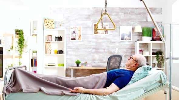 Old Retired and Disabled Man Lying in a Hospital Bed in a Nursing Home