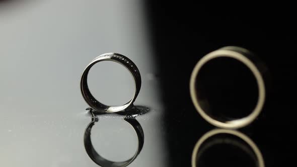 Wedding Rings on Black, White Water Surface. Groom Ring Rolling To Bride's Ring
