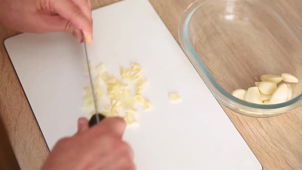 Girl Cuts Garlic with a Knife on the Board. Woman in the Kitchen Chopped Peeled Garlic