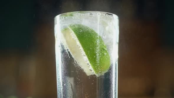 Transparent ice cubes fall into a glass of sparkling water with slices of lime