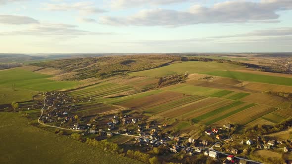 Aerial view of countryside village with small houses among green trees with farm fields 