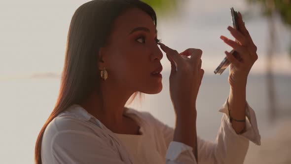 Young Woman Adjusting Eye MakeUp Using Compact Mirror