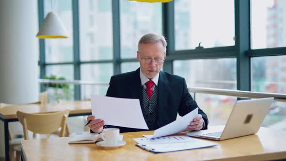 Businessman is reading a printed report or document while sitting at the table