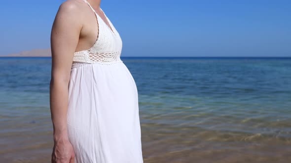 Beauty of Pregnancy Period Woman with Big Baby Bump in White Dress Walking on the Sunny Ocean Coast