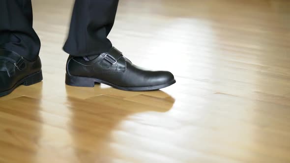 Legs of a man in black shoes dancing elements of dubstep on the brown floor background.