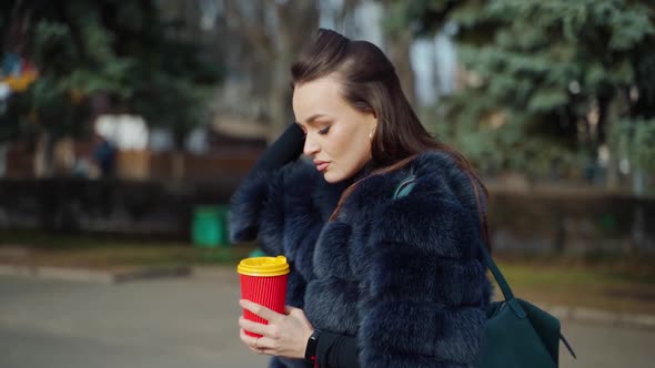 Side view of a beautiful woman outdoors. Pretty girl in luxury fur coat walking in the park with a p