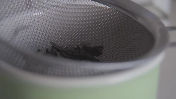 Extreme Close-up of Dried Tea Leaves Falling Into Strainer in the Cup