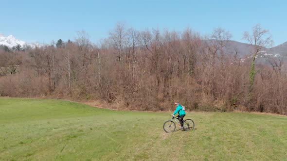 Aerial slow motion: man having fun by riding mountain bike in the grass on sunny day, scenic alpine