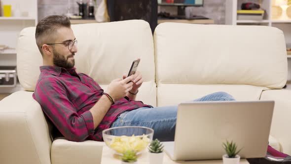 Handsome Young Man Relaxing on Couch Using His Phone