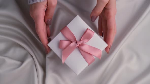 Female Hands Giving and Taking White Gift Box with Pink Ribbon