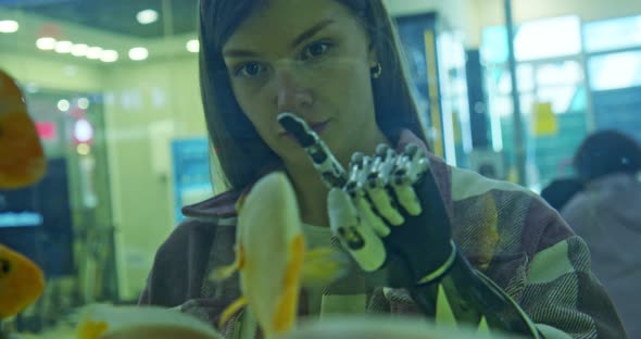 Portrait of a Young Woman with a Disability Who Touches a Glass Aquarium with a Bionic Hand Looking