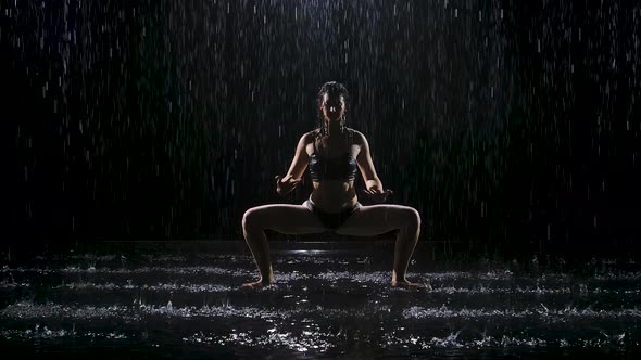 Woman Doing Yoga Exercises in the Pouring Rain in a Dark Studio. Spotlight Illuminates the Surface