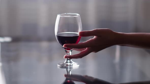 Graceful female hand takes a glass of red wine from the table, light background