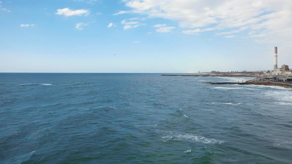 Mediterranean sea and shoreline aerial shot flying backwards over gentle rolling waves on a sunny da