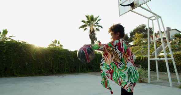 an AfricanAmerican Boy in a Colorful Shirt Playing with a Basketball on a Green Playground Among