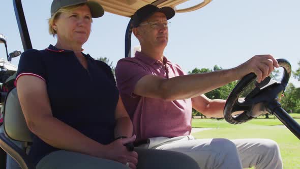 Caucasian senior couple driving a golf cart with clubs on the back at golf course