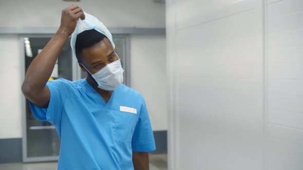 Portrait of Tired Surgeon Removing Safety Cap and Mask Walking in Hallway After Long Surgery