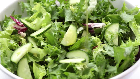 Pouring oil on a green salad in white bowl.