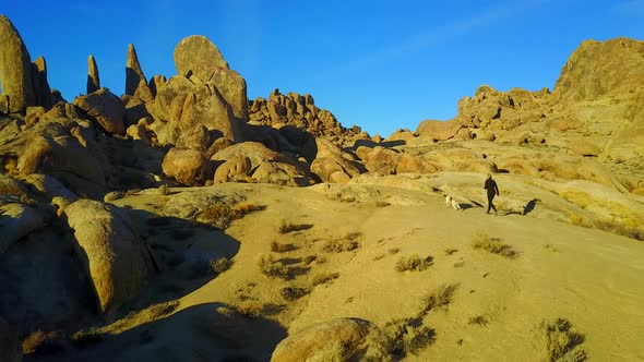 Aerial drone view of a woman hiking with her dog in a rocky desert landscape.