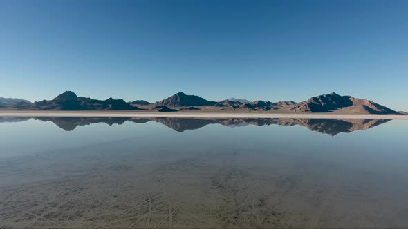 An aerial drone shot reveals smooth water covering the Bonneville Salt Flats and reflects distant mo