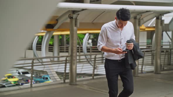 Asian young business man walking up on stair going to work and chat on mobile phone outdoor.