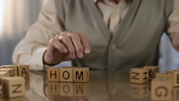 Aged Man Making Word Home of Wooden Cubes on Table, Alzheimer Disease Therapy