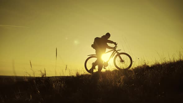 The Silhouette of the Mountain Bicycle Rider on the Hill with Bike at Sunset. Sport, Travel and